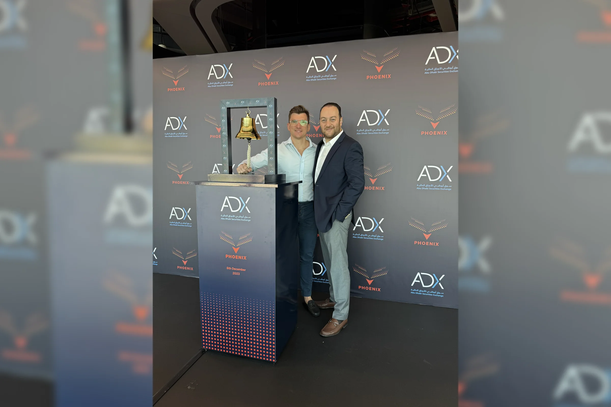 Two Phoenix Group colleagues at the ceremonial bell on the Abu Dhabi Securities Exchange step-and-repeat, 5 December 2023