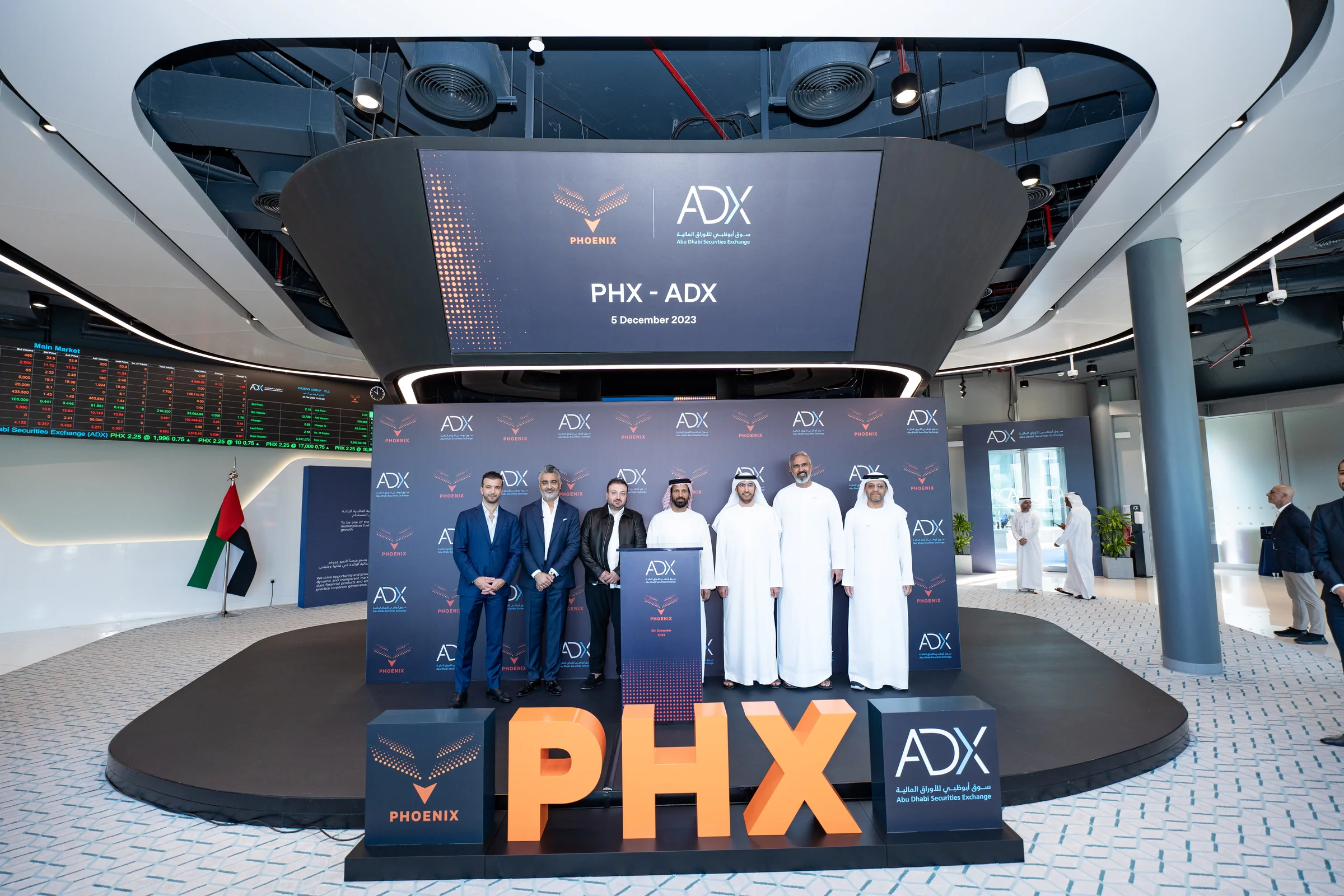 Phoenix Group and Abu Dhabi Securities Exchange representatives on the listing podium beside the PHX letters, 5 December 2023