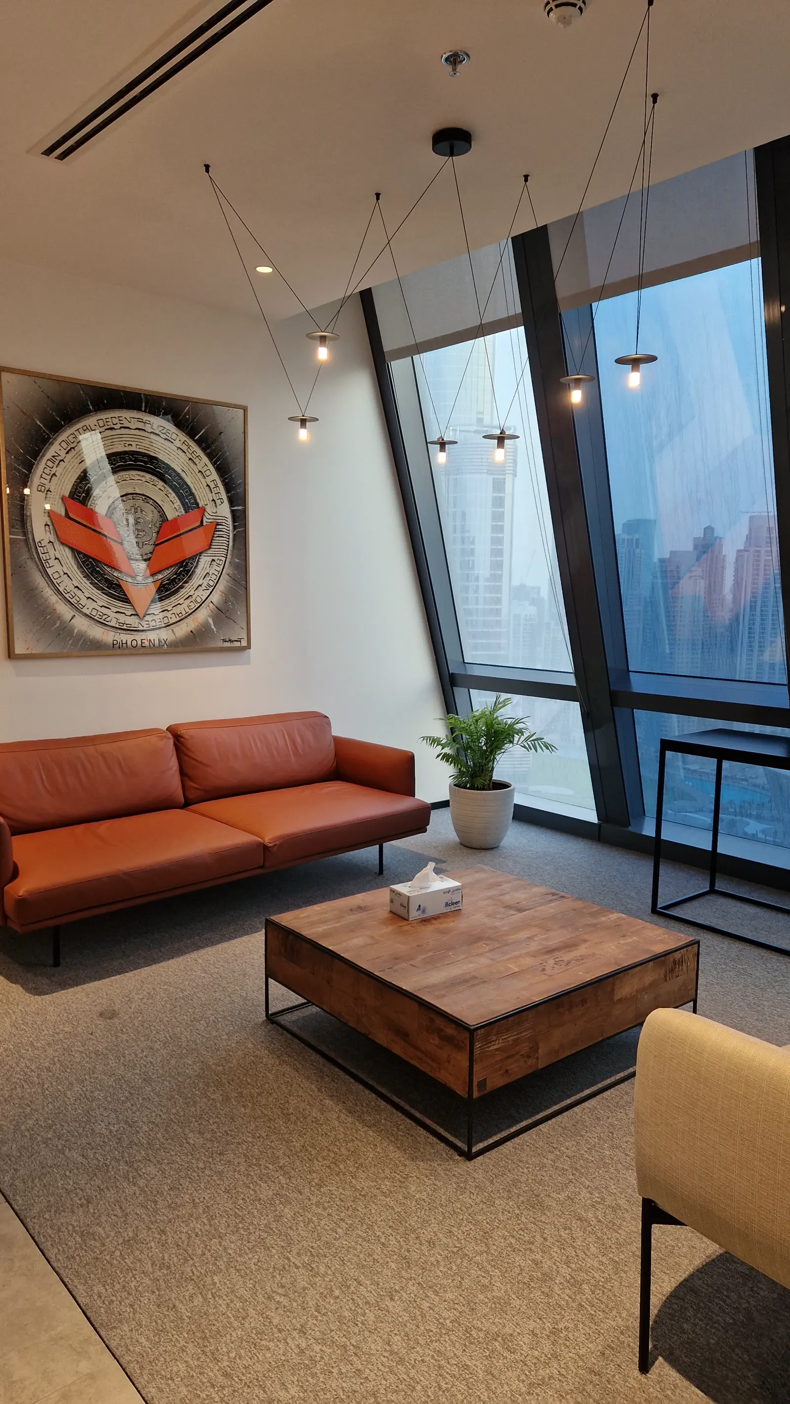 Phoenix Group brand artwork framed in the office lounge, with the Dubai skyline through the window