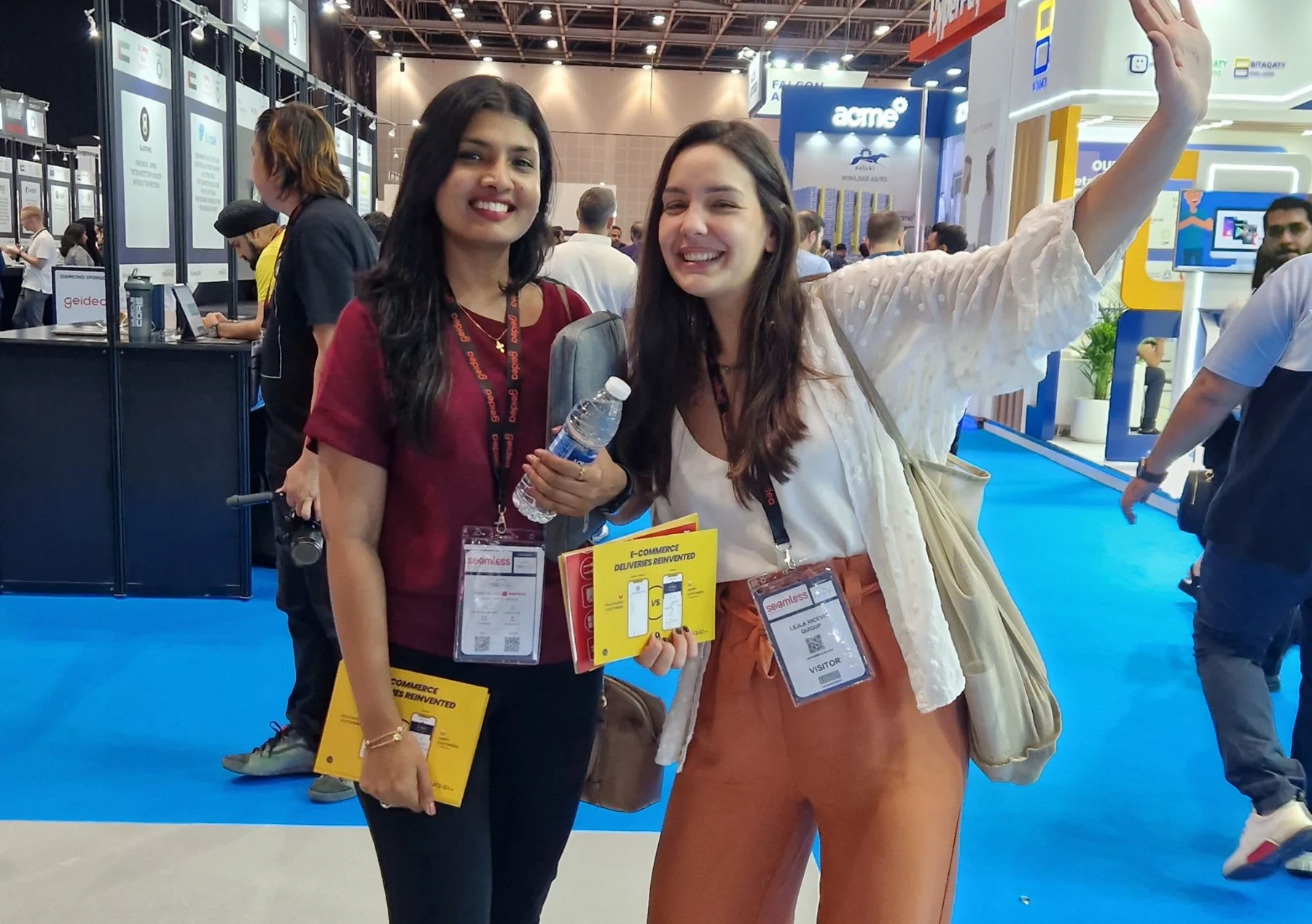 Two members of the Quiqup team at Seamless Middle East in Dubai, each holding the yellow E-Commerce Deliveries Reinvented postcard